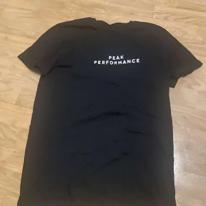Svart t-shirt från Peak Performance - Säljer en svart t-shirt från Peak Performance med vit text på bröstet. T-shirten är kortärmad och har en klassisk passform. Sparsamt använd. Pris går att diskutera vid snabb affär.