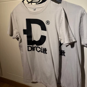 Vit t-shirt från DirtCult - Säljer en vit t-shirt från DirtCult med stort svart tryck på framsidan. Man kan köpa båda tröjorna för 300kr och båda är i storlek S, ena tröjan så är trycket lite bort nött men annars så är dom i bra skick.
