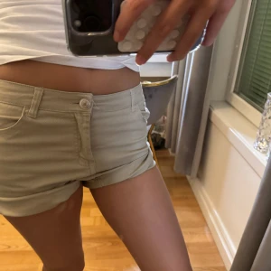 Beige shorts - Snygga beige shorts med låg midja och knappdetalj framtill. Perfekta för varma sommardagar med en stilren look. De har en klassisk design med fickor och är gjorda i ett bekvämt material. Vet inte vilket märke, men säljer för de inte kommer till användning!