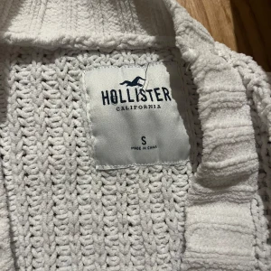 Vit stickad kofta från Hollister - Mysig vit stickad kofta från Hollister med knappar framtill. Perfekt för kyliga dagar med sin ribbade design och långa ärmar. En klassisk och stilren look som passar till det mesta.
