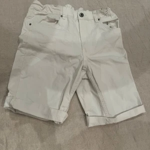 Vita shorts från SNRLRY - Snygga vita shorts från SNRLRY med uppvikta ben och knappstängning. Perfekta för varma dagar med en stilren look. De har både fram- och bakfickor för extra funktionalitet.