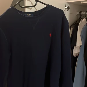 Mörkblå tröja från Ralph Lauren - Säljer en stilren mörkblå tröja från Ralph Lauren med det klassiska röda logotypbroderiet på bröstet. Tröjan har långa ärmar och en rund halsringning. Tveka inte på att höra av dig