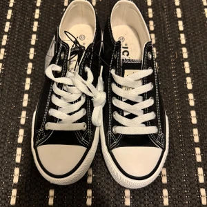 Svarta sneakers med vita detaljer - Snygga svarta sneakers med vita snören och detaljer. Skorna har en klassisk design med låg profil och vita sulor. Perfekta för en avslappnad stil.