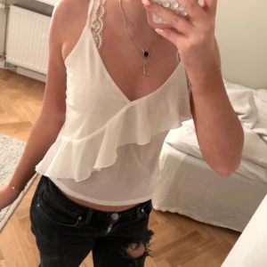 Vit ärmlös topp med volangdetaljer - Säljer en söt krämvit topp från H&M med volangdetaljer framtill, säljs inte längre!🩷