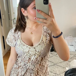 Beige spetsblus - Säljer en vacker beige spetsblus med blommigt mönster. Blusen har korta ärmar och en v-ringad design. Den är knytbar i ryggen för en justerbar passform. Perfekt för en elegant look.