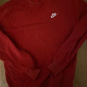 Röd tröja från Nike - Säljer en snygg röd tröja från Nike med deras klassiska logga i vitt på bröstet. Tröjan har långa ärmar och är perfekt för en sportig look. Passar bra till både träning och vardag.