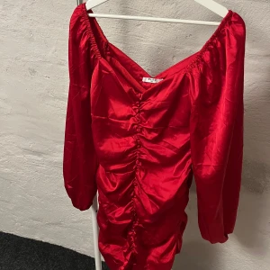 Röd klänning med rynkdetaljer - Snygg röd klänning från NA-KD med rynkdetaljer framtill. Klänningen har långa ärmar och en v-ringad design som ger en elegant look. Perfekt för att liva upp garderoben med en färgklick.