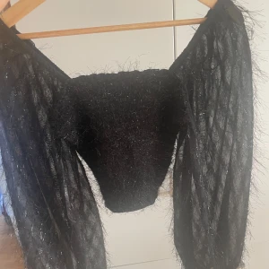 Svart glittrig tröja - Säljer en unik svart tröja med glittriga detaljer. Tröjan har långa ärmar och en fluffig textur som ger en cool look. Perfekt för att sticka ut på festen!