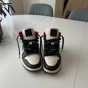 Nike Air Jordans i svart, vitt och rött - Snygga Nike Air Jordans i klassisk färgkombination av svart, vitt och rött. Skorna har en hög modell med snörning och ikoniska detaljer som Jumpman-loggan på plösen. Perfekta för dig som vill ha en stilren och sportig look.