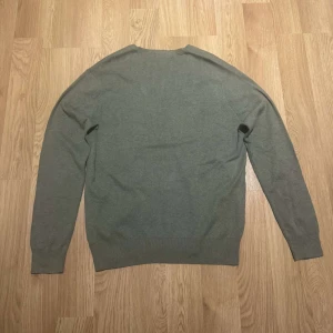 Grön tröja från Polo Ralph Lauren - Säljer en stilren grön tröja från Polo Ralph Lauren i mjuk bomull. Tröjan har en v-ringad hals och ett diskret broderat logotypmärke på bröstet. Perfekt för en avslappnad och snygg look.