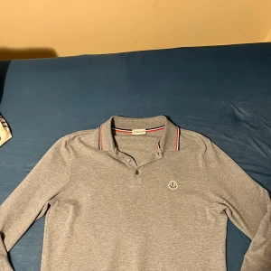 Grå pikétröja från Moncler - Säljer en stilren grå pikétröja från moncler den är köpt från Nk för 3800kr för några månader sedan men den är för liten för mig storlek L men sitter som M fråga om du har några funderingar! Tar imot rimliga byten. Skicket är typ 9-10 
