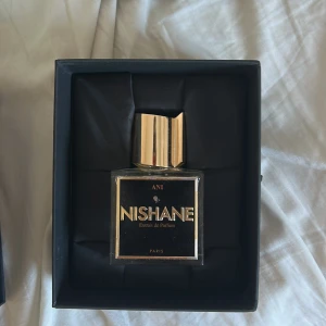 Nishane Ani Extrait de Parfum - Säljer en lyxig Nishane Ani Extrait de Parfum. Flaskan är fyrkantig med en elegant guldfärgad kork. Parfymen har en rik och djup doftprofil med toppnoter av bergamott och rosépeppar, hjärtnoter av svartvinbär och basnoter av vanilj och mysk. Perfekt för den som älskar unika och sofistikerade dofter.