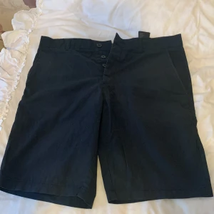 Svarta shorts med knappar - Snygga svarta shorts med knappar framtill. Perfekta för en avslappnad stil. De har en klassisk design med fickor på sidorna och en knappdetalj bak. Passar bra till både t-shirt och skjorta.