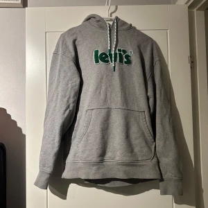 Grå hoodie från Levi's - Säljer en grå hoodie från Levi's i storlek XS. Den har en avslappnad passform med en stor ficka framtill och en justerbar huva. Perfekt för en casual look.