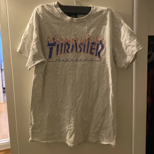 Grå T-shirt från Thrasher - Säljer en grå T-shirt från Thrasher med det ikoniska flammande logotyptrycket i blått och orange på framsidan. Pris kan diskuteras!
