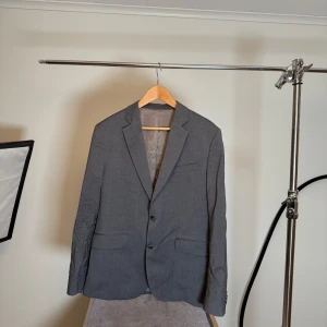 Grå kostym från J. Lindeberg - Snygg grå kostym från J. Lindeberg i normal passform. Kavajen har två knappar och byxorna har en klassisk design. Perfekt för formella tillfällen. Är rynkig men hel och väldigt fin. Behöver bara strykas