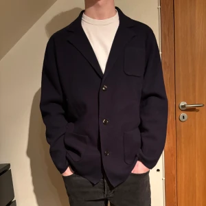 Mörkblå stickad kavaj från John Henric - Säljer en mörkblå stickad kavaj från John Henric. Modellen är 183cm och bär storlek L