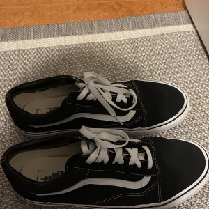 Svarta sneakers från Vans - Säljer ett par klassiska svarta Vans sneakers med vit sula och snörning. Skorna har den ikoniska vita sidoremsan och är perfekta för en avslappnad stil.