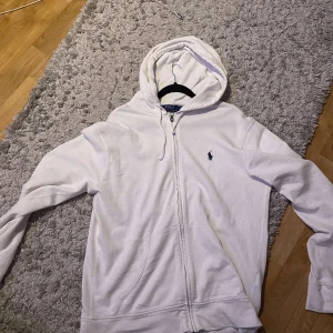 Vit hoodie från Ralph Lauren - Säljer en klassisk vit hoodie från Ralph Lauren med dragkedja och den ikoniska loggan broderad på bröstet. köpte för en månad sen typ, har knappt använt den inga fläckar. Nypris 1799kr. 