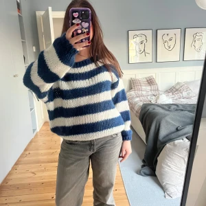 Randig stickad tröja från Design by Si - Mysig stickad tröja från Design by Si i blått och vitt. Tröjan har ett randigt mönster och långa ärmar. Tröjan är har några lösa trådar där bak. Använts ett väldigt få antal gånger 