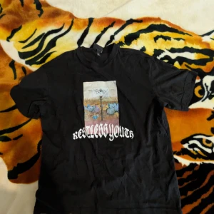 Baggy svart t-shirt från H&M med tryck - Säljer en svart t-shirt från H&M med ett coolt tryck på framsidan och texten 'Restless Youth'. T-shirten är i relaxed fit och tillverkad av 100% bomull. Perfekt för en avslappnad stil.