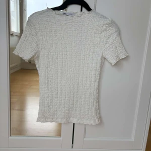 Vit och svart ribbad topp från Zara - Säljer två ribbade toppar från Zara i vitt och svart. Båda topparna har korta ärmar och en enkel design som passar perfekt till vardags. Materialet är stretchigt och bekvämt.