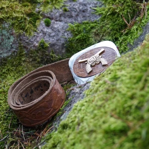 Brunt skärp med pistoldetalj - Säljer ett coolt brunt skärp med en unik spänne som har en pistoldetalj i silver och trä🤠 Skärpet har ett ingraverat mönster längs hela remmen och är tillverkat i skinn🔥 Perfekt för att ge en western-look till din outfit❌Defekter - Mindre repor och missfärgning på baksidan av spännet. Synligt slitage på lädret med några bläckmärken nära hålen. Lätta repor runt pistoldesignen, men överlag i gott vintageskick. Från 40-talet. Total längd, 98 cm, användbar längd, 92.5 cm.