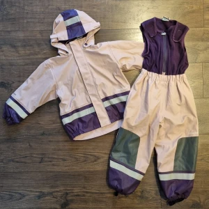 Lila regnställ från Didriksons - Säljer ett lila regnställ från Didriksons med avtagbar huva och reflexdetaljer. Jackan har dragkedja och muddar vid ärmslut. Byxorna har justerbara hängslen och förstärkta knän. 100% vind och vattentätt med svetsade sömmar. Varmt fleecefoder. Galon även en bit in i ärm och benslut. Perfekt för regniga dagar! 🌧️  Behövs byta de avtagbara fothällorna.