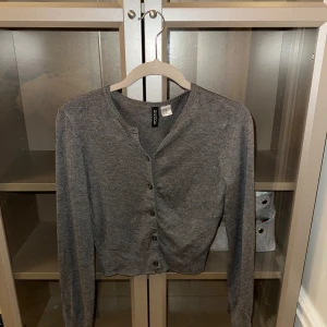 Grå kofta från Gina Tricot - Säljer en stilren grå kofta från Gina Tricot. Den har långa ärmar och knappar framtill. Perfekt för lager-på-lager och passar till många olika outfits.