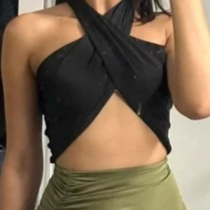 Svart omlott topp - Snygg svart omlott topp med ett unikt korsat mönster framtill. Toppen är ärmlös och har en stilren design som passar perfekt för en kväll ute. Den är tillverkad i ett mjukt och bekvämt material.