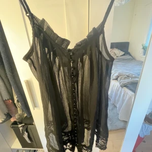 Svart transparent linne från Vila - Säljer en svart transparent linne från Vila med knappar framtill. Den är lite längre men ändå inte riktigt en klänning 💞