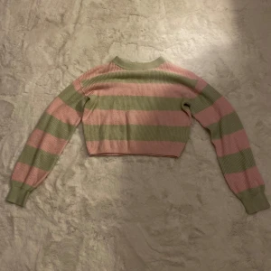 Randig croppad tröja från H&M - Säljer en söt randig tröja från H&M i grönt och rosa. Tröjan är croppad och har långa ärmar med ribbade muddar. Perfekt för en avslappnad stil.