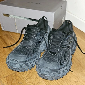 Defenders/Bouncers från Balenciaga - Säljer ett par svarta sneakers från Balenciaga med robust sula och snörning. Skorna har en modern design med detaljer i syntetmaterial och mesh för extra andningsförmåga. Perfekta för en trendig look. Obs äkta!