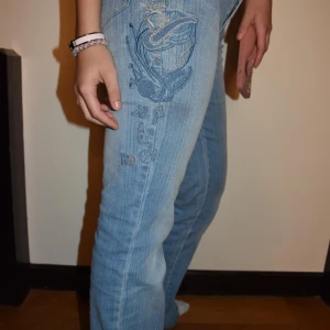 Blåa bootcut jeans med coola detaljer 🩵 - Snygga ljusblå bootcut jeans med jätte coola detaljer på bakfickan och sidan. Säljer då dom tyvärr inte kommer till användning. Innebredslängd: 82cm Midja: 36cm sitter perfekt på modellen som är 175cm 💕