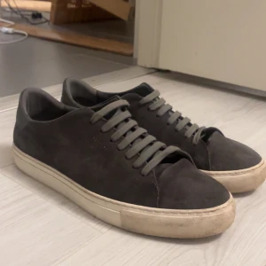 Gråa sneakers från Axel Arigato - Snygga gråa sneakers från Axel Arigato i mocka med snörning. Funkar hur bra som helst behövs bara en tvätt