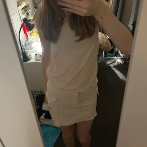 Beige/vit kjol från H&M - Snygg beige kjol från H&M med praktiska fickor och dragkedja framtill. Kjolen har en kort längd och är perfekt för en stilren look. Tillverkad i ett bekvämt material som passar bra till olika tillfällen.
