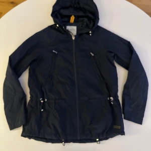 Svart vindjacka från Peak Performance - Säljer en svart vindjacka från Peak Performance i storlek XS. Jackan har en praktisk huva och dragkedja framtill. Perfekt för blåsiga dagar med justerbara snören i midjan och vid ärmslut. En stilren och funktionell jacka för utomhusaktiviteter.