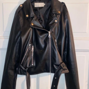 Svart skinnjacka från NLY Trend, Nelly  - Säljer en snygg svart skinnjacka från NLY Trend (Nelly)  i storlek 38. Jackan har en cool bikerstil med dragkedjor och knappar i silver. Den är croppad och har ett bälte i midjan för extra edge. Perfekt för höst och vår! 🖤 knappt använd 