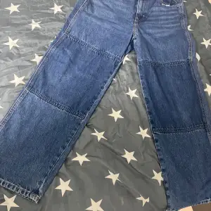 Säljer ett par snygga blå jeans med vida ben. De är i bra skick och perfekta för en avslappnad stil. Jeansen har en klassisk design med fem fickor och knappgylf. Perfekta för både vardag och fest!