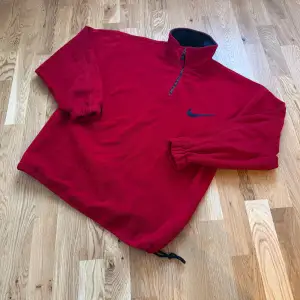 Säljer en röd fleece tröja från Nike i storlek XL men sitter som L. Den har en halv dragkedja och elastiska muddar vid ärmsluten. Perfekt för kyliga dagar med sin mjuka och varma känsla. Nike-loggan är broderad i svart på bröstet. Passar både för träning och vardag.