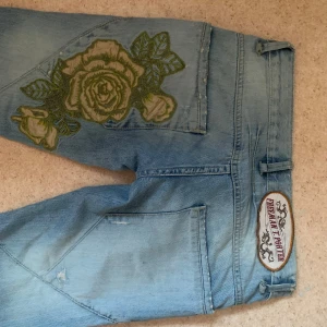 Ljusblå jeans med rosbroderi - Säljer ett par ljusblå jeans från Freeman T Porter i bra skick. De har ett stort, snyggt rosbroderi på baksidan och en låg midja. Passformen är flare/bootcut. Midjemåttet är 37cm och jeansen har ingen stretch. De är väldigt lågmidjade så bör passa runt storlek 34 då de så lågmidjade. Innerbensmåttet är 79cm. De är för långa på mig som är 163. Och alldeles för små på mig som brukar bära storlek 28. På lappen på jeansen står storlek 25.  Kan diskutera priset vid snabbt köp!
