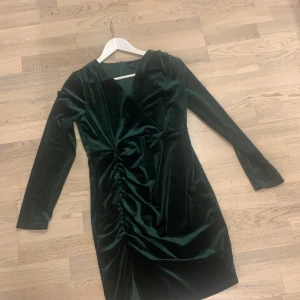 Mörkgrön sammet klänning - Snygg mörkgrön klänning i sammet  och rynkdetaljer framtill. Den har långa ärmar och en dragkedja bak. Perfekt för höst- och vinterfester! 🎄