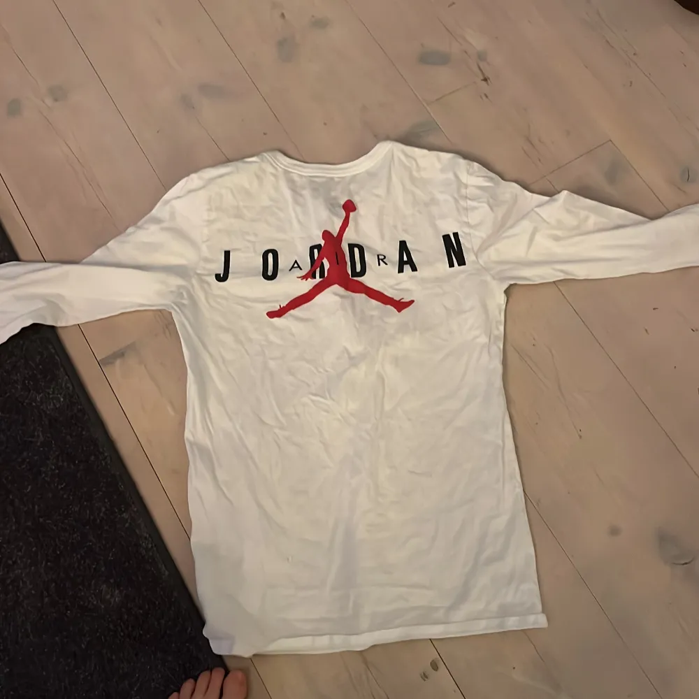 Säljer en vit långärmad tröja från Jordan med det klassiska Jumpman-logotypen i rött och svart på ryggen. Perfekt för en sportig och avslappnad stil. Tröjan är i bra skick och passar perfekt för höst och vår.. Tröjor & Koftor.