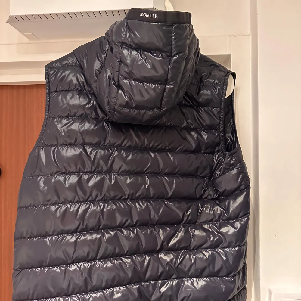 Säljer en snygg svart dunväst från Moncler i mycket bra skick. Västen har en quiltad design med dragkedja och en praktisk huva. Perfekt för höst och vår när du vill hålla dig varm och stilren. Passar både till vardags och lite finare tillfällen. Köpt från garmsmarket. Har ett litet litet hål som är lagat med en liten lapp som sitter på sista bilden. Syns inte alla, där av priset. Jackor.