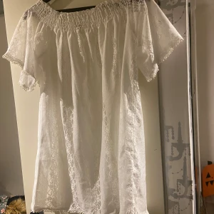 Vit spetsklänning - Säljer en superfin vit spetsblus med offshoulder-design. Perfekt för alla fester! Blusen har korta ärmar och en luftig passform som gör den bekväm att bära. Den romantiska spetsen ger en elegant touch. Passar perfekt till både vardag och festliga tillfällen. 🌸