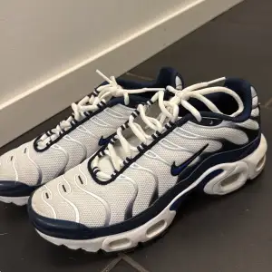 Säljer ett par Nike Air Max Plus i vitt och blått. Skorna har en snygg design med vågiga linjer och den klassiska Nike(tn)-loggan på sidan. De är i mycket bra skick och perfekta för både vardag och träning. Skön passform med snörning för bästa komfort. Skorna är i nyskick endast använda en gång. Hör gärna av er om ni funderar över något! 