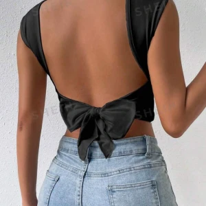 Svart croppad topp med öppen rygg  - Snygg svart croppad topp med en stilren design. Toppen har en öppen rygg med en knytning som ger en extra touch. Perfekt för sommarens fester eller en utekväll. Materialet är mjukt och bekvämt, vilket gör den skön att bära hela dagen.