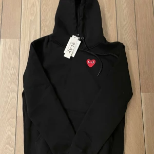 Svart hoodie från Comme des Garçons Play - Säljer en grymt fräsch svart hoodie från Comme des Garçons play i storlek S/Xs. Tröjan är helt oanvänd därför i nyskick, alla tags är kvar! Ny pris ligger på 2500kr. Vid frågor så tveka inte på att höra av er! Vid snabb affär kan priset diskuteras!