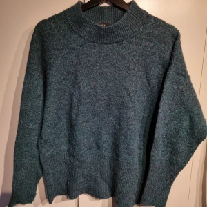 Mörkgrön stickad tröja - Säljer en supermysig mörkgrön stickad tröja med hög krage. Perfekt för kyliga höst- och vinterdagar. Tröjan har en lös passform och långa ärmar, vilket gör den extra bekväm. Passar perfekt till jeans eller leggings för en avslappnad look.