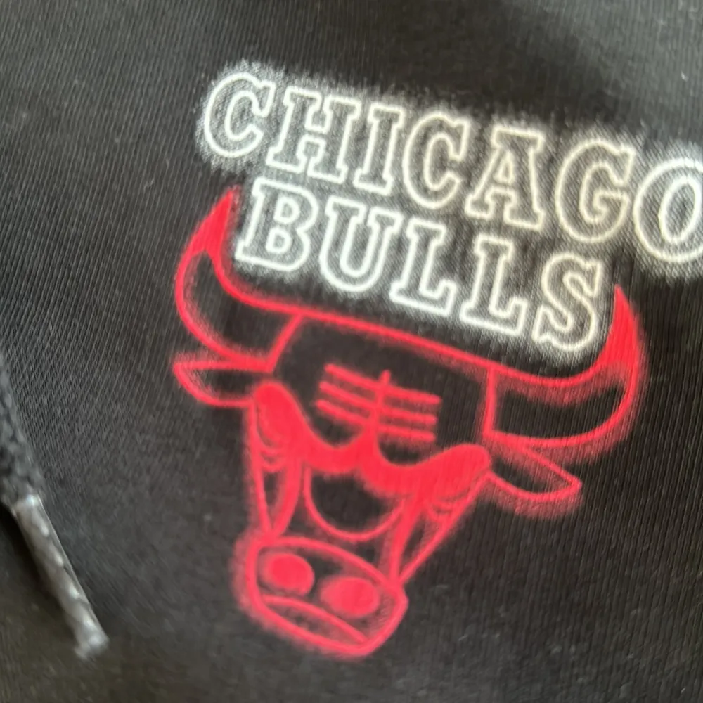 Säljer en svart hoodie från New Era med Chicago Bulls-logga i rött och vitt på bröstet. Den har en stor ficka fram och justerbar huva. Perfekt för basketfans eller bara för en chill stil. 🏀. Tröjor & Koftor.